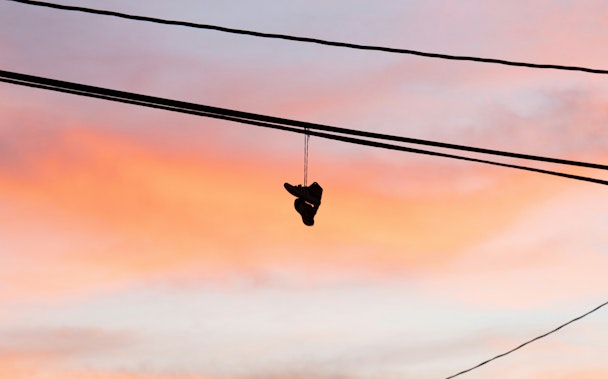 A pair of trainers or sneakers hangs over a telephone wire by the laces against a dawn or dusk sky A pair of trainers or sneakers hangs over a telephone wire by the laces against a dawn or dusk sky