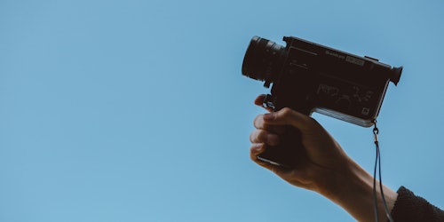Person holding video camera against blue background Person holding video camera against blue background